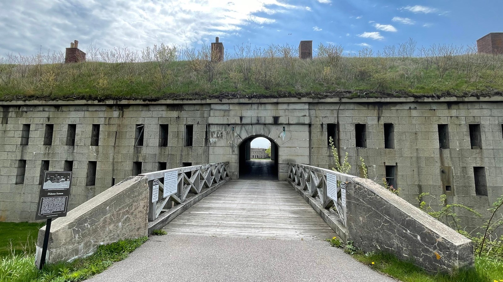Drawbridge leading to a fortress with an archway. Fortress has two rows of windows on either side.