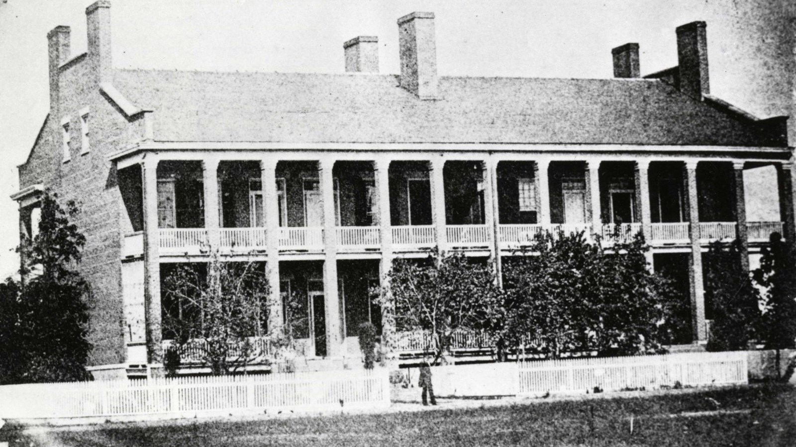Black and white photo 2 story brick building with 13 columns supporting a balcony and proch.