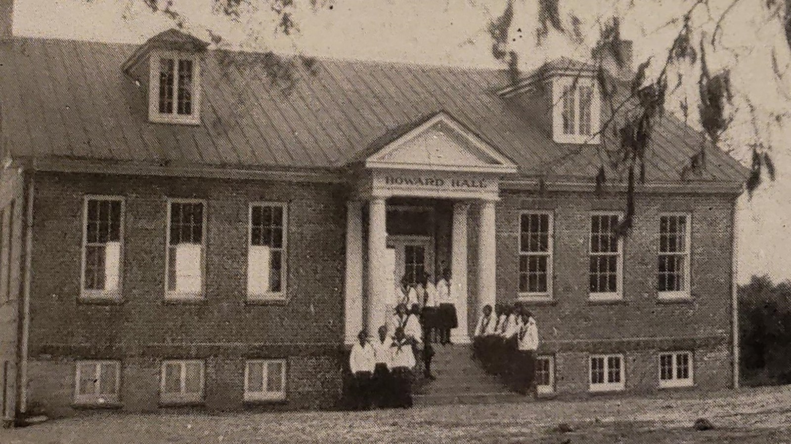 A group of students outside a brick building with white porch.