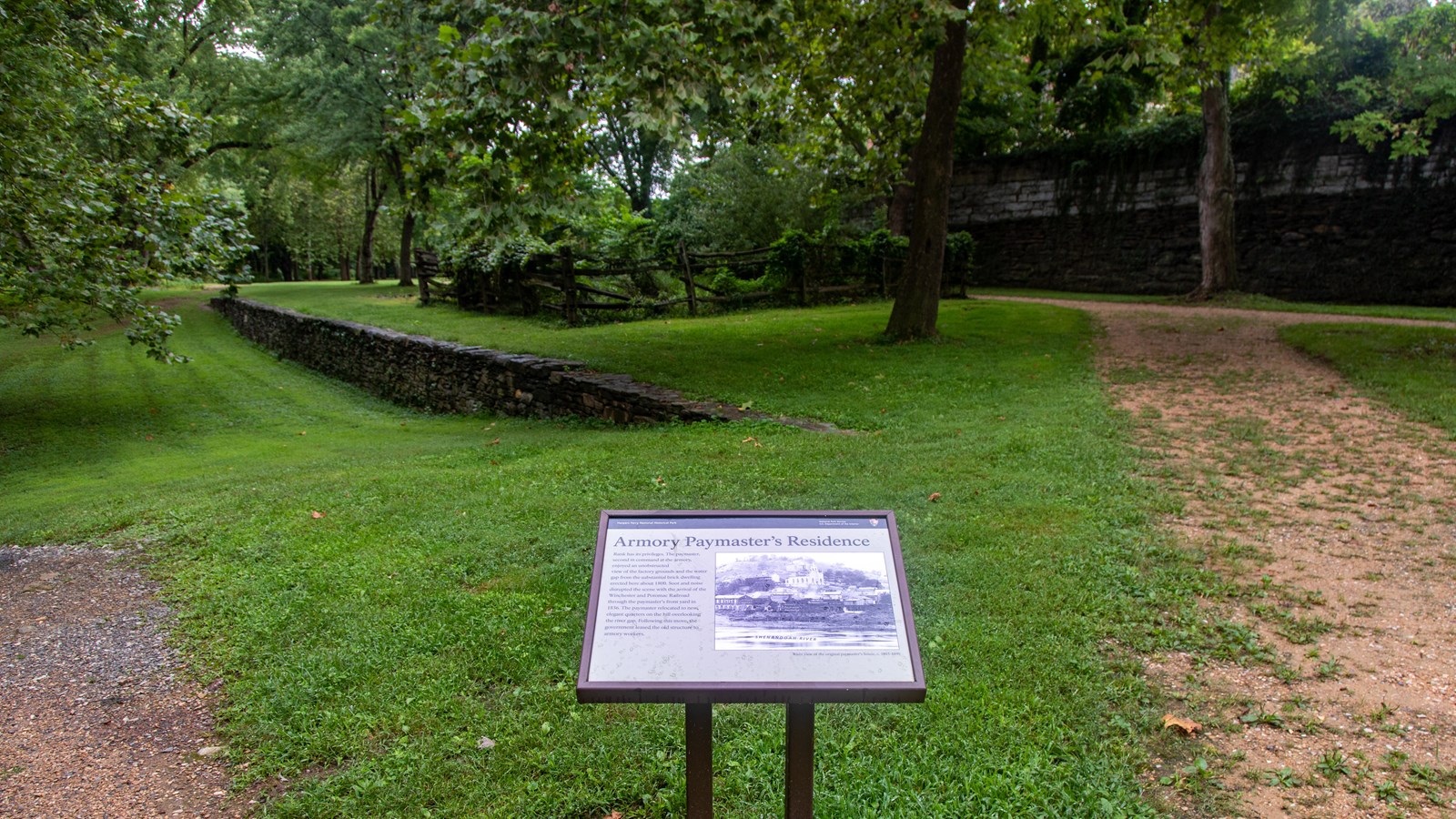 A information panel wayside in front of a grassy trail.