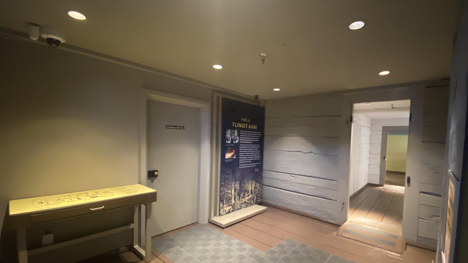 small grey painted room with a table map, shut door, and sign on a wall and a doorway on another