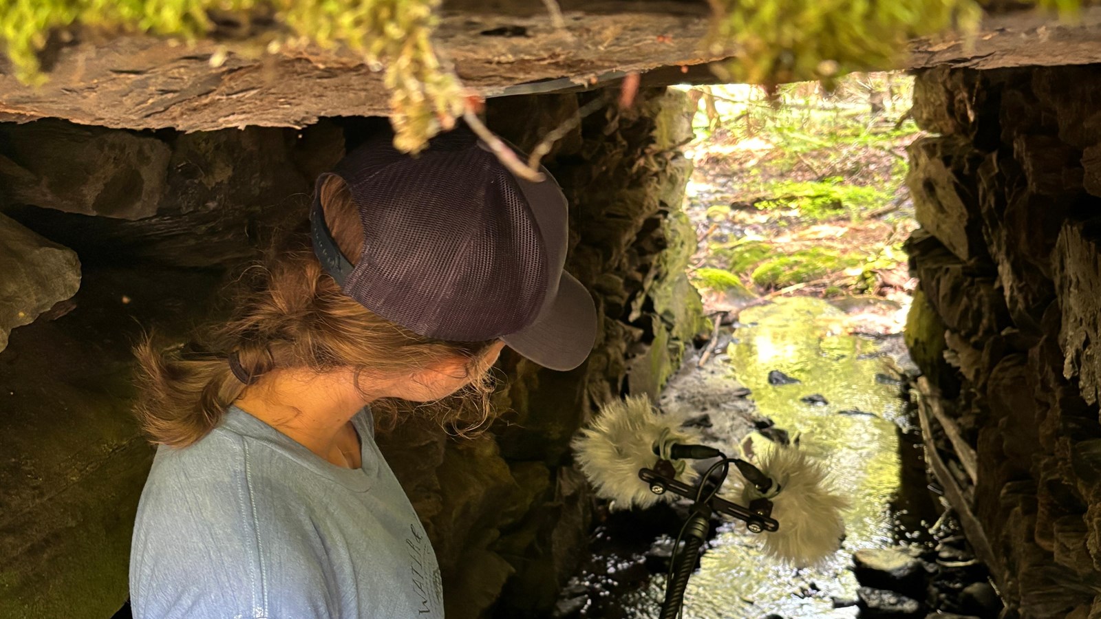 person stands holding boom microphone inside stone culvert