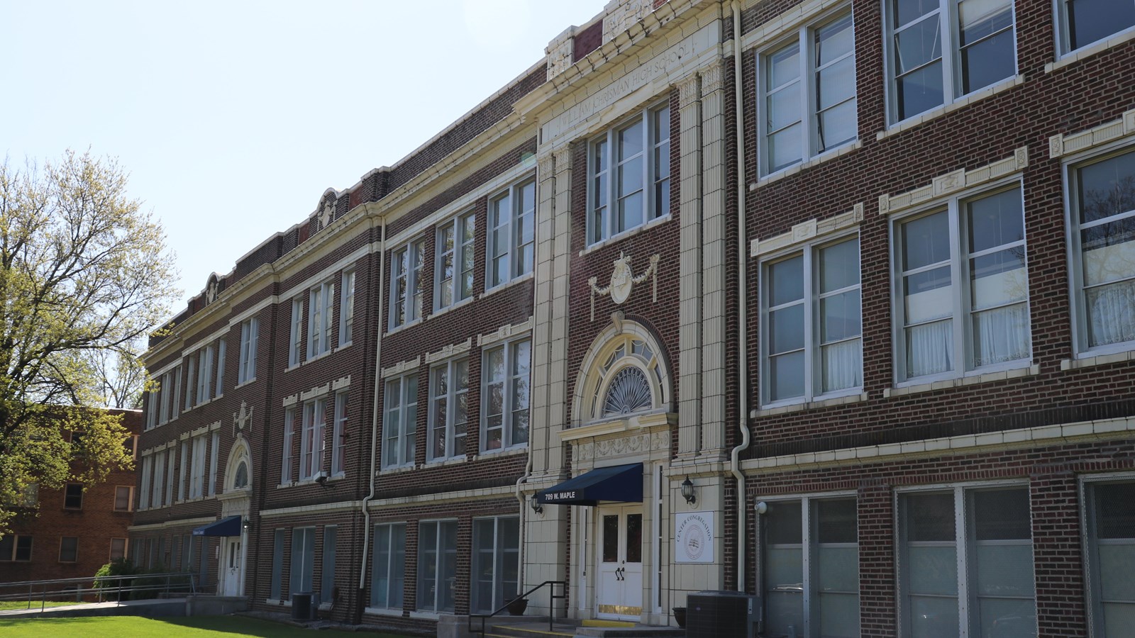 A three story brick building with rows of windows and two entrances with blue awnings.