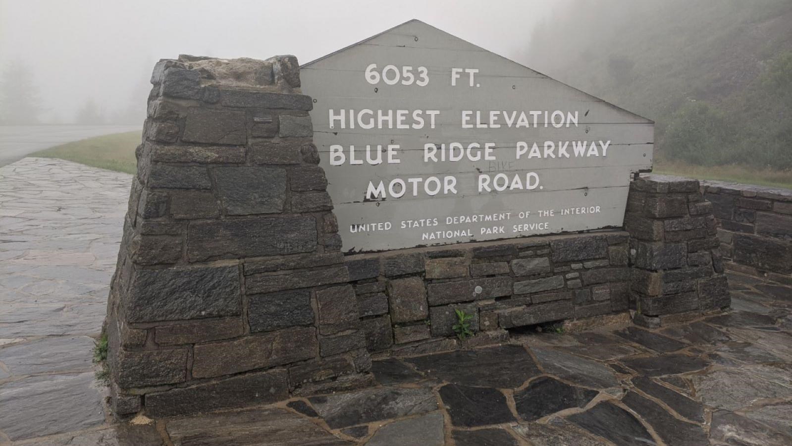 Gray wooden sign framed by stone designating the highest point on the Parkway