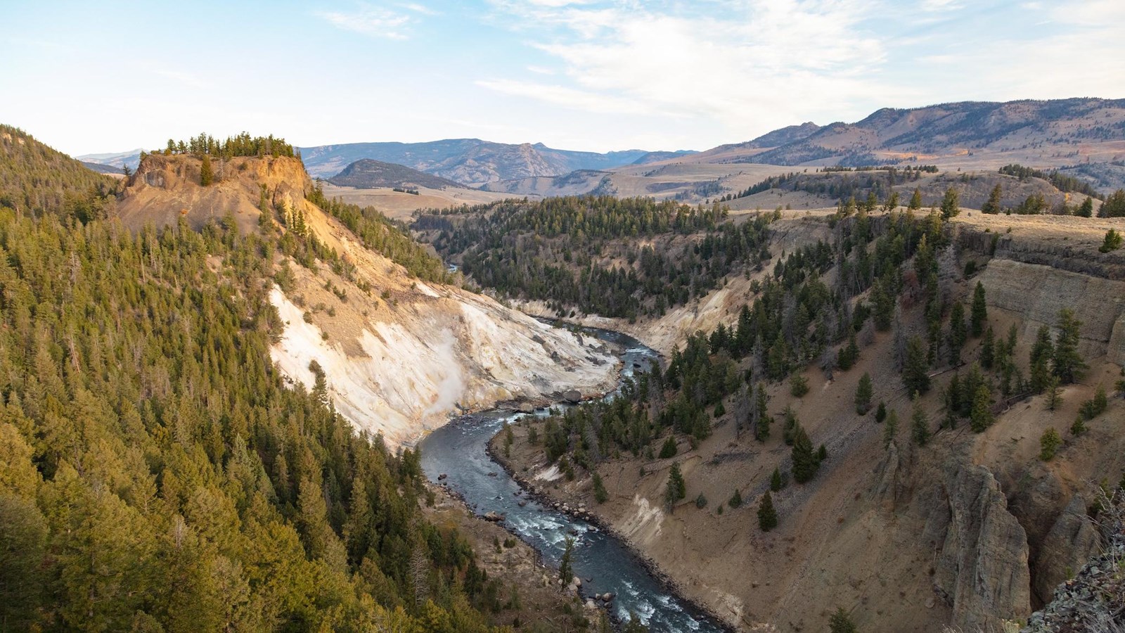 A river runs through a canyon. Steam is released from a thermal area near a bend in the river.