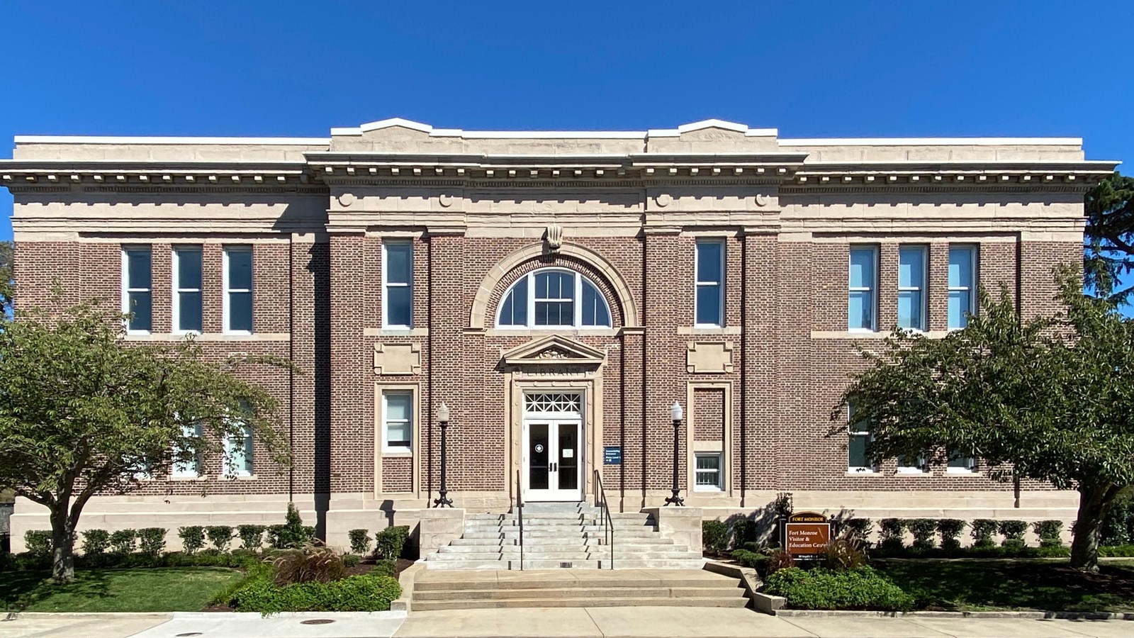 Brown Flemish Bond brick building with limestone foundation and trim under a cloudless deep blue sky