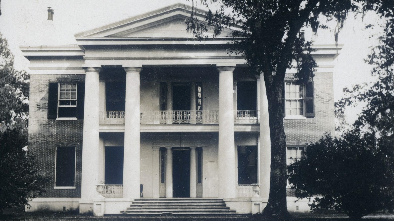 Black and white image of Greek Revival style mansion featuring four doric columns.