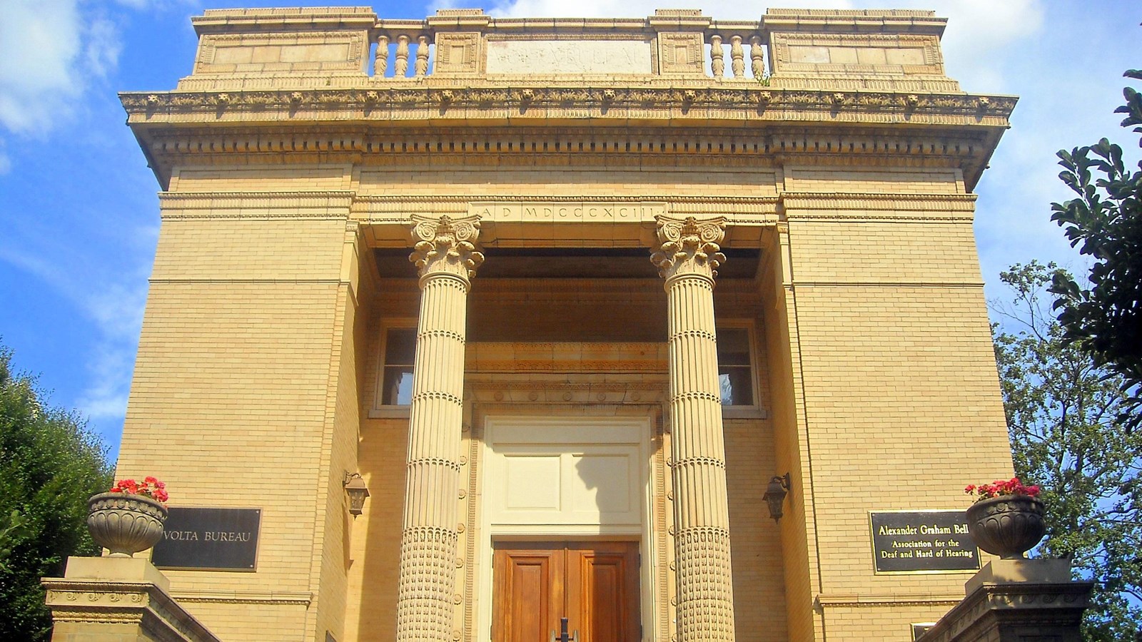 A large, yellow stone building with two columns at the portico.