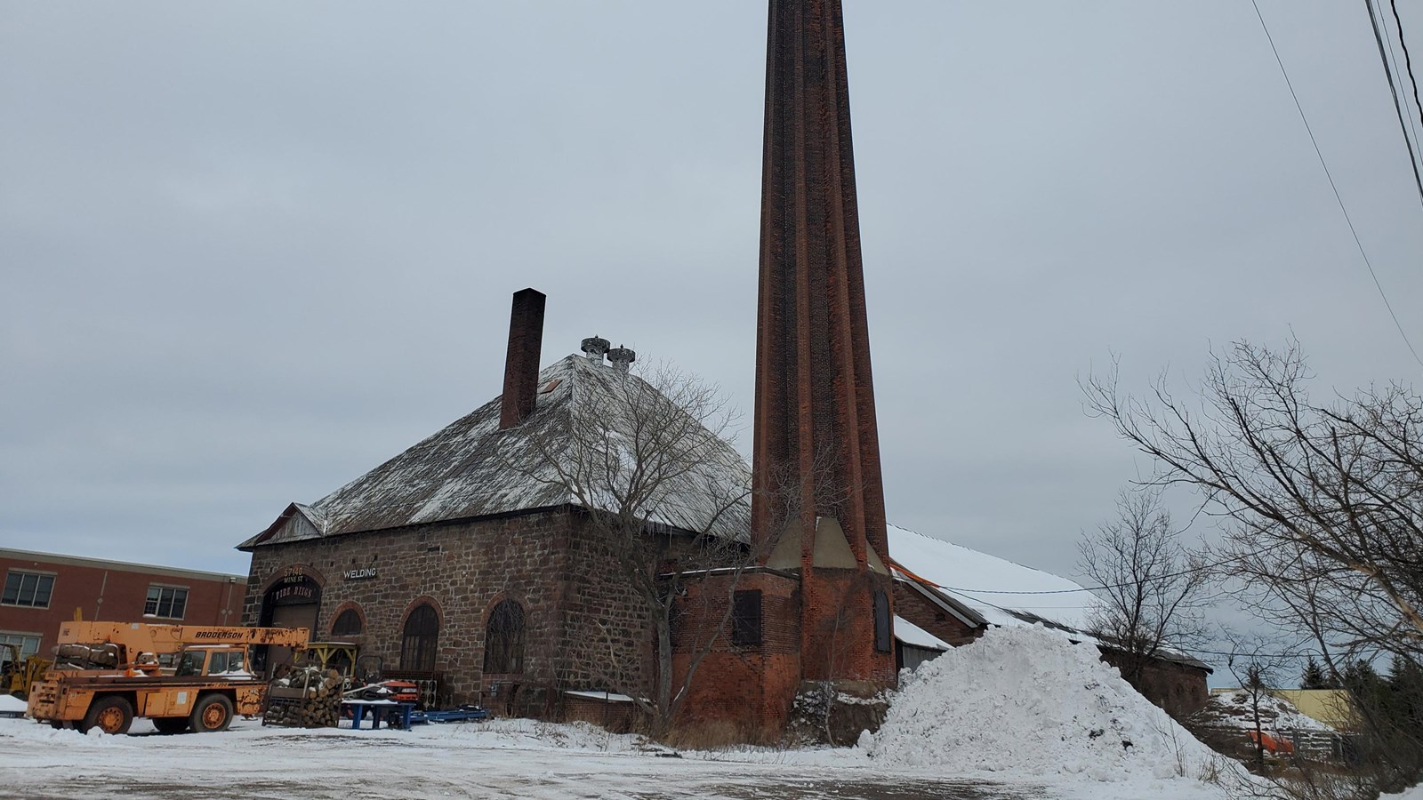 Winter scene of poor-rock and red sandstone building with a red brick smokestack in the foreground.