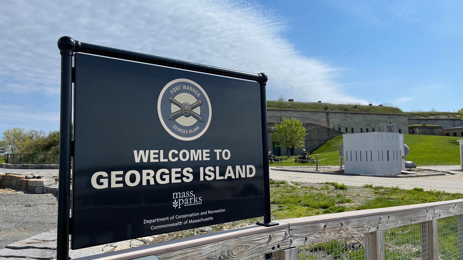 Black sign welcoming visitors to Georges Island. Fort seen in the background.
