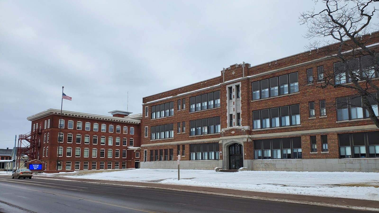 Winter scene of red brick school building with many windows and brick encased digital sign in front.