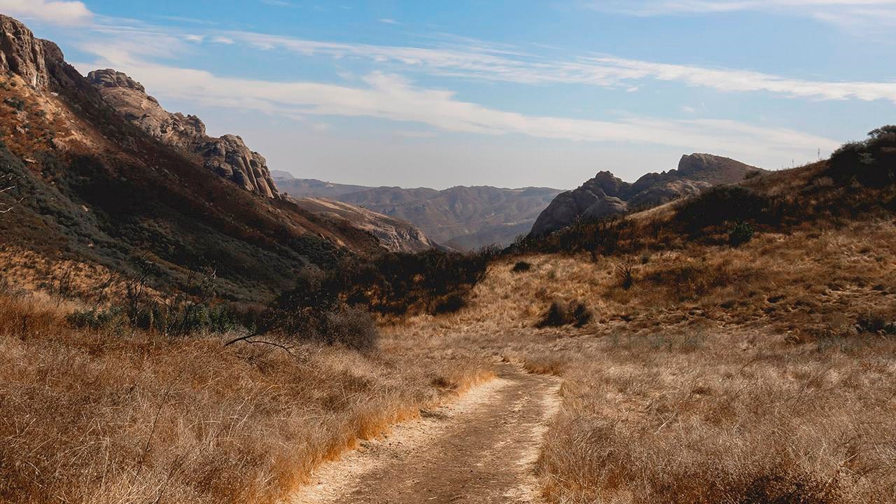 Wispy clouds in a bright sky over a trail leading into mountains.