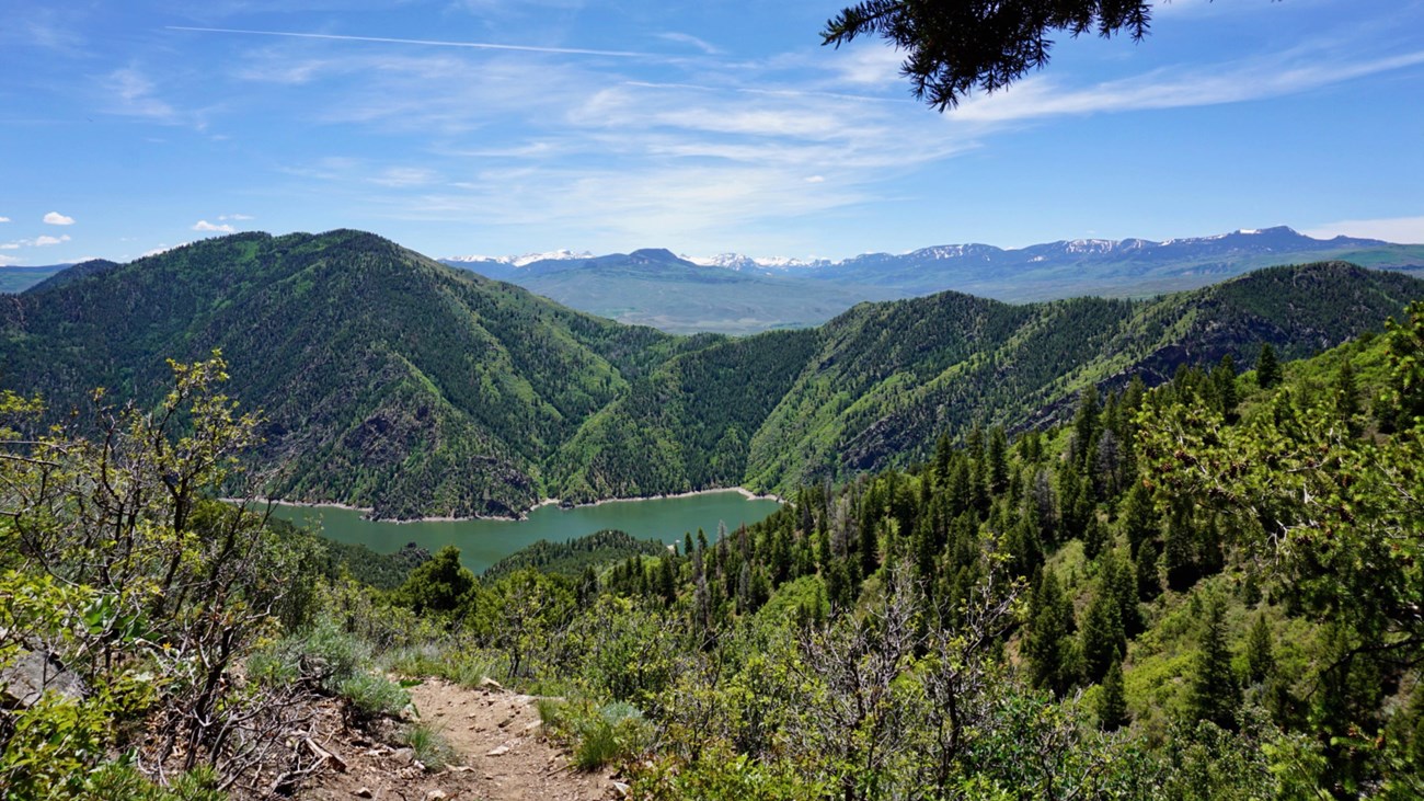 A trail with a view of mountains and overlooking a dam in the distance