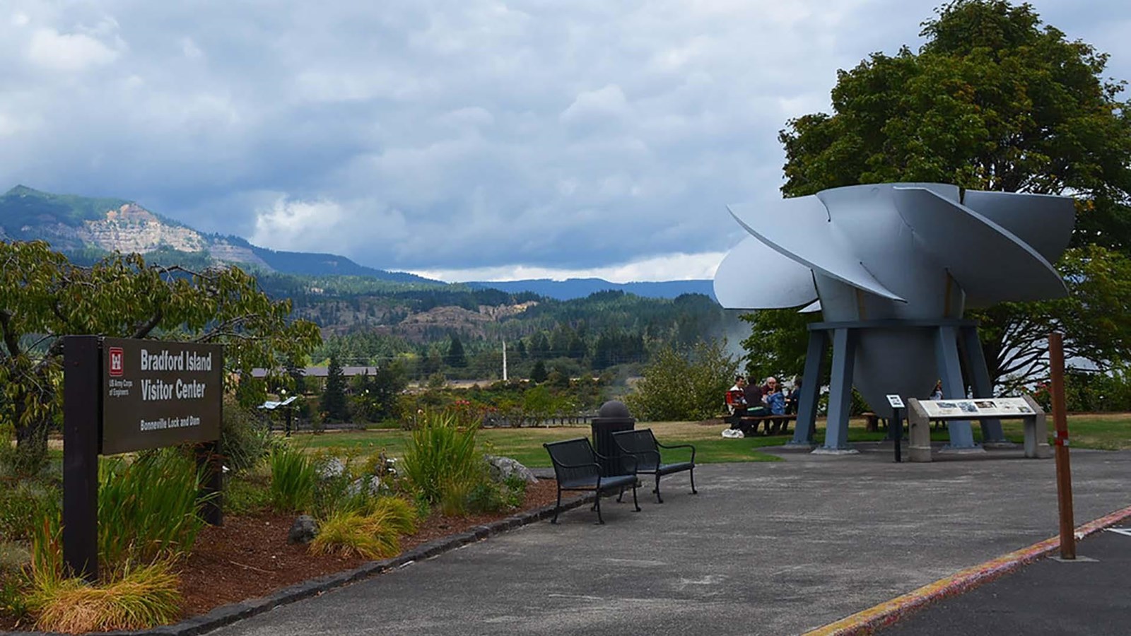 A sidewalk leads up to a large turbine on display used for hydroelectric power.