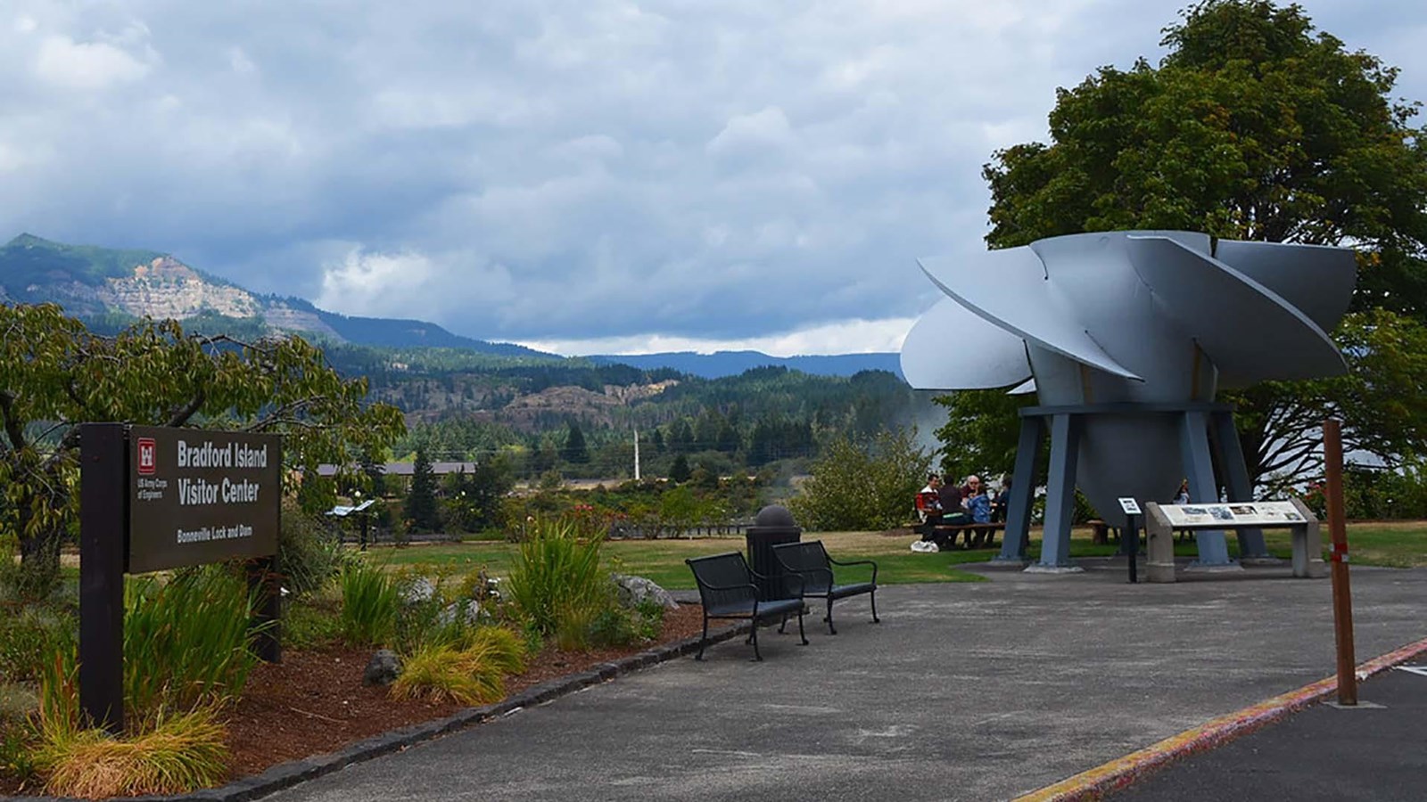 A sidewalk leads up to a large turbine on display used for hydroelectric power. 