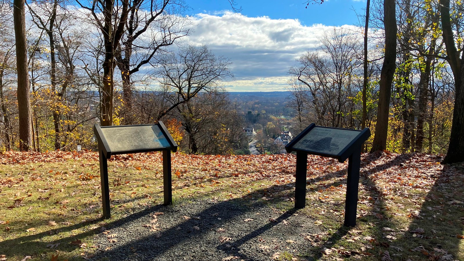 Two wayside panels next to each other by a gravel path on a hill overlooking a valley.