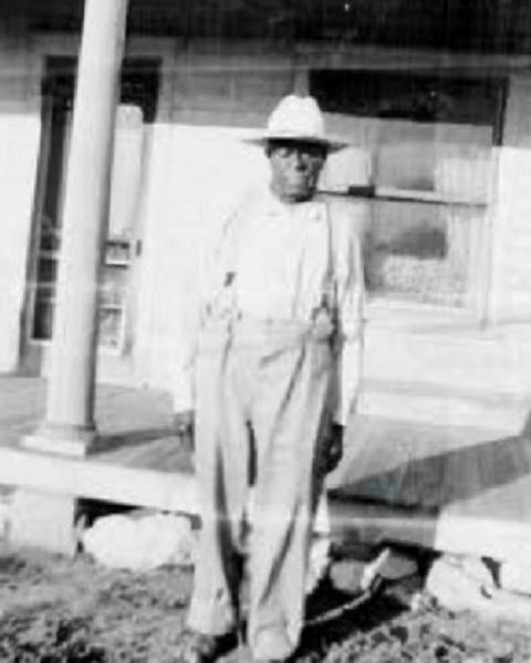 Black and white photo of man standing in front of front porch of house