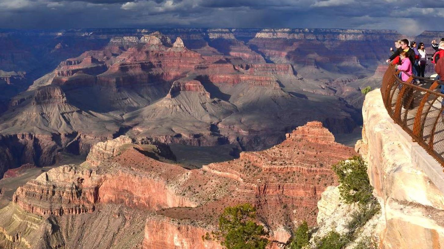 People behind guardrails at a scenic overlook viewing a colorful landscape of peaks and cliffs.