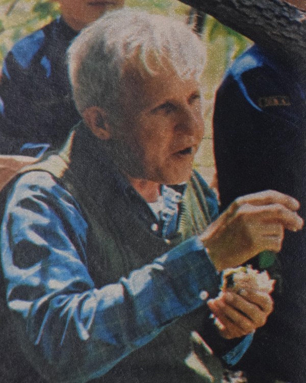 A white-haired man seated beneath trees near two young boy scouts