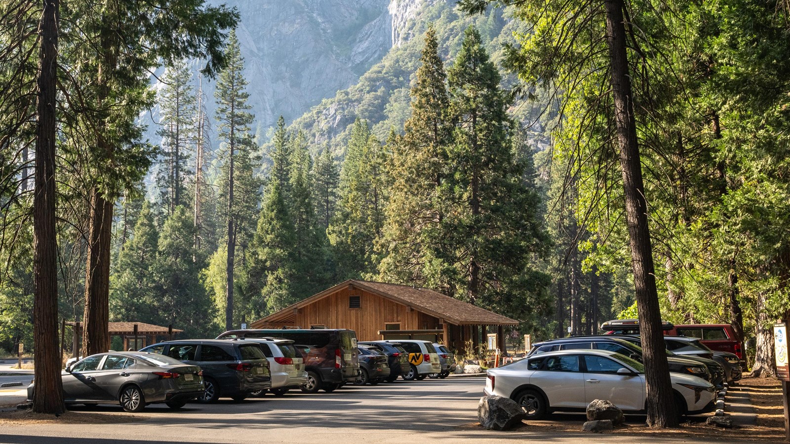 Vehicles line a paved parking area with a large granite formation in the background