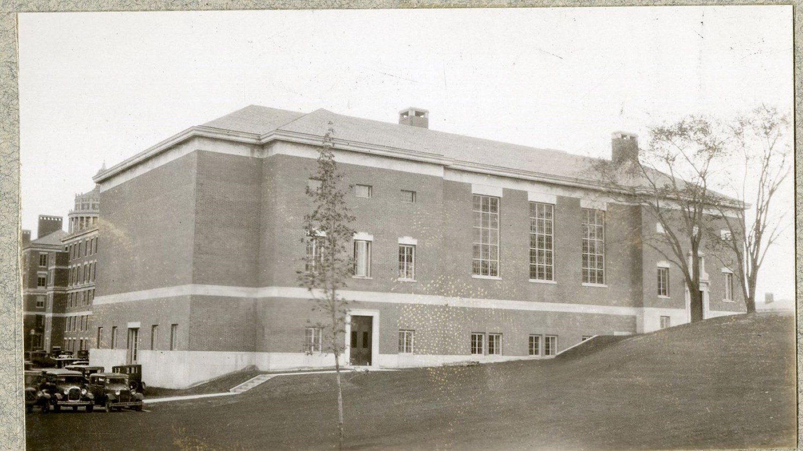 Black and white of large building on grassy hill with trees on side of building
