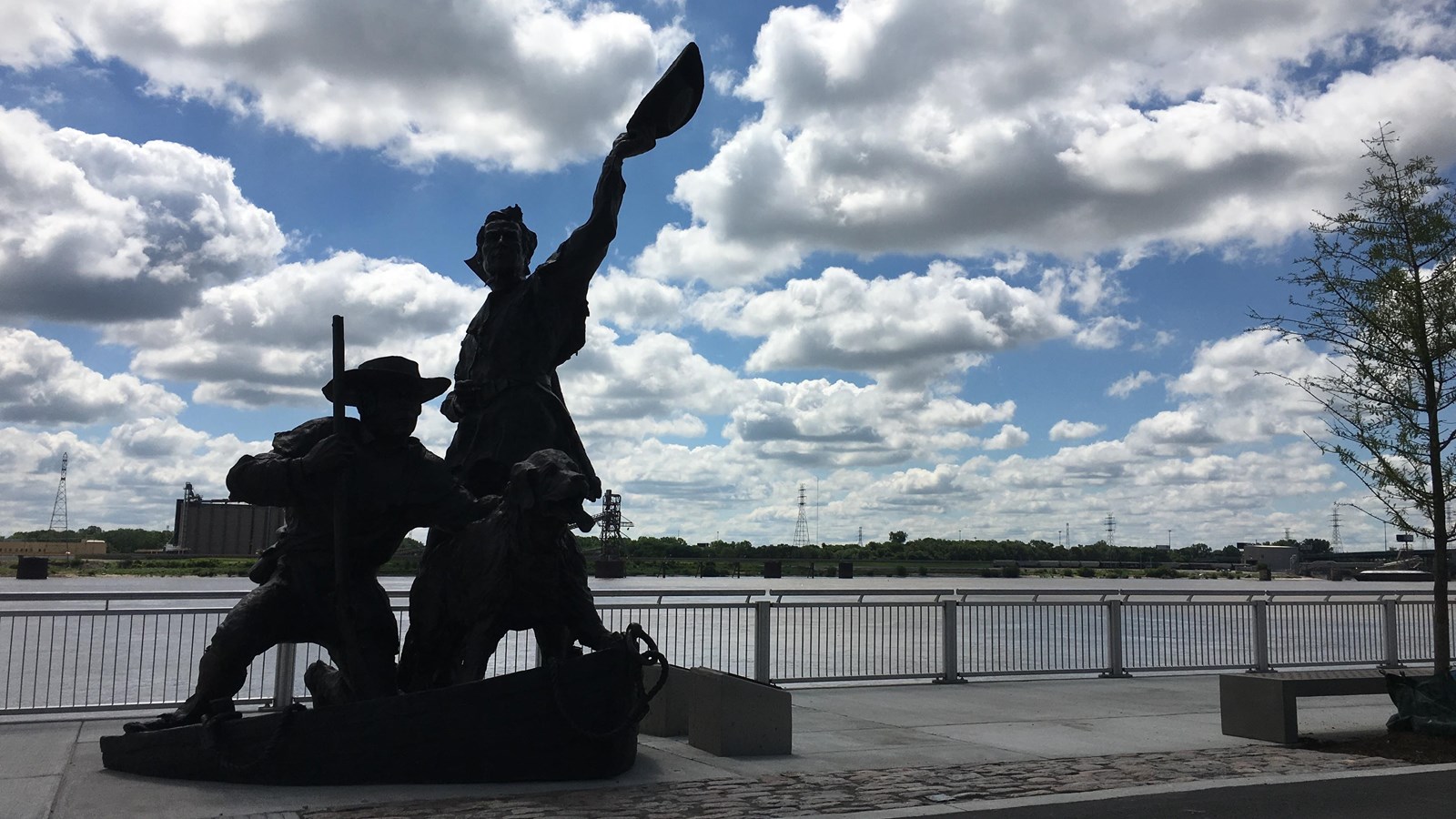 Image of a large statue of two men and a dog silhouetted against a blue sky with many clouds