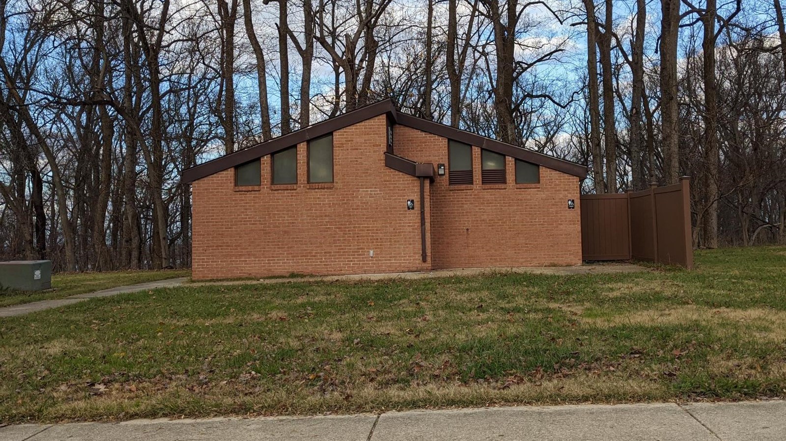 Photo of the main parking lot bathroom.  Concrete sidewalk in front and trees behind.