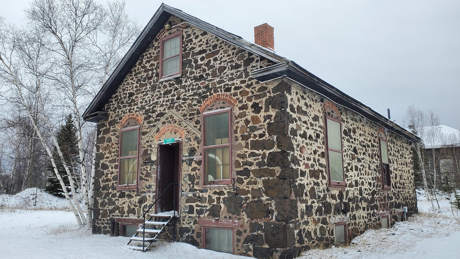 Winter scene of a dark brown poor-rock building with wide light grey mortar lines.