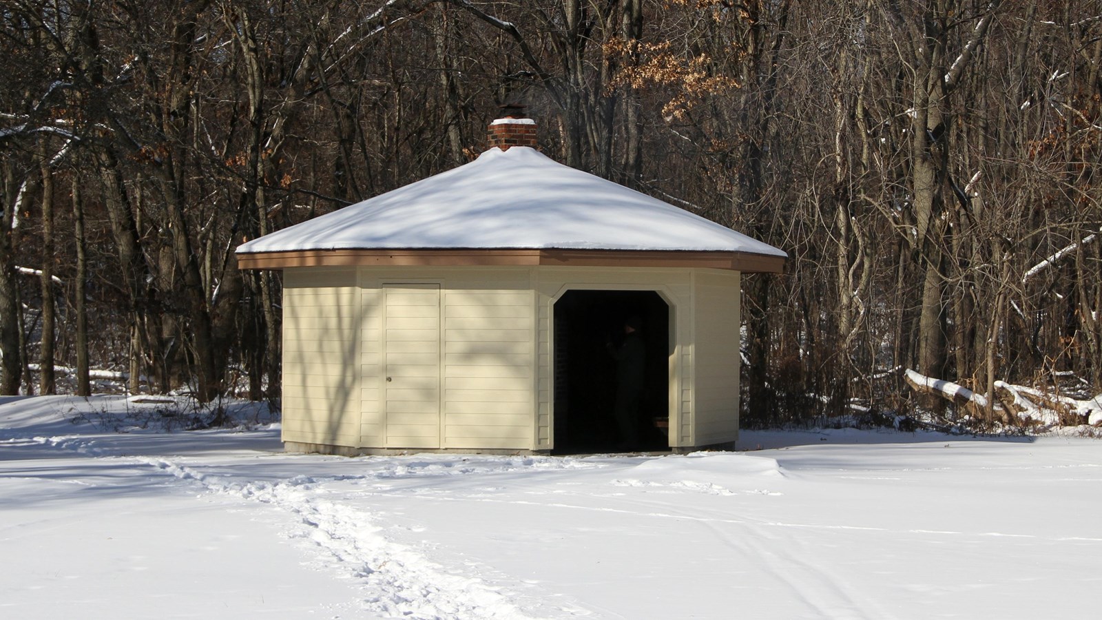 Snow covers the ground. A white and brown hut with a large opening provides warmth for skiers.