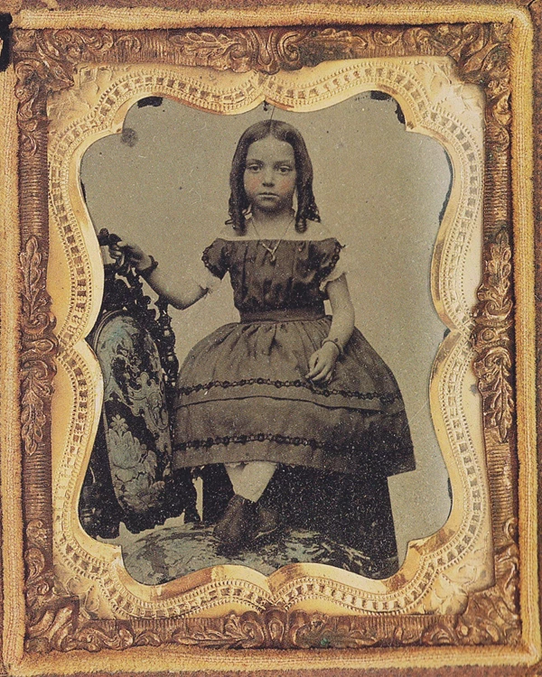 A framed 1800s photograph shows a little girl in a dress posing on a chair.