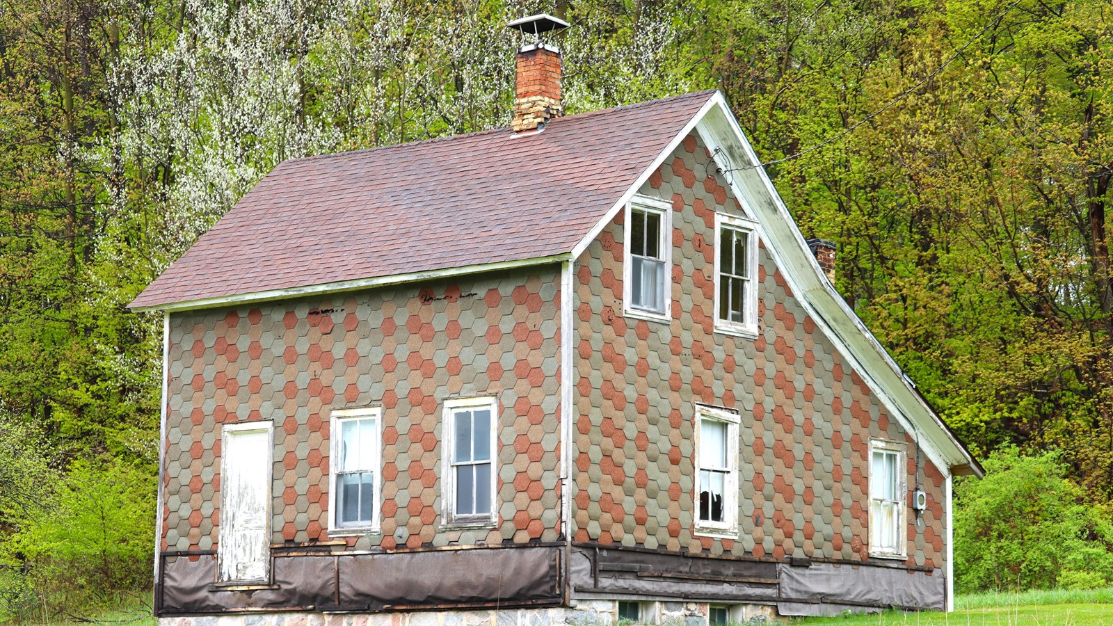 An old house with colorful octagonal siding, sitting on a stone foundation.