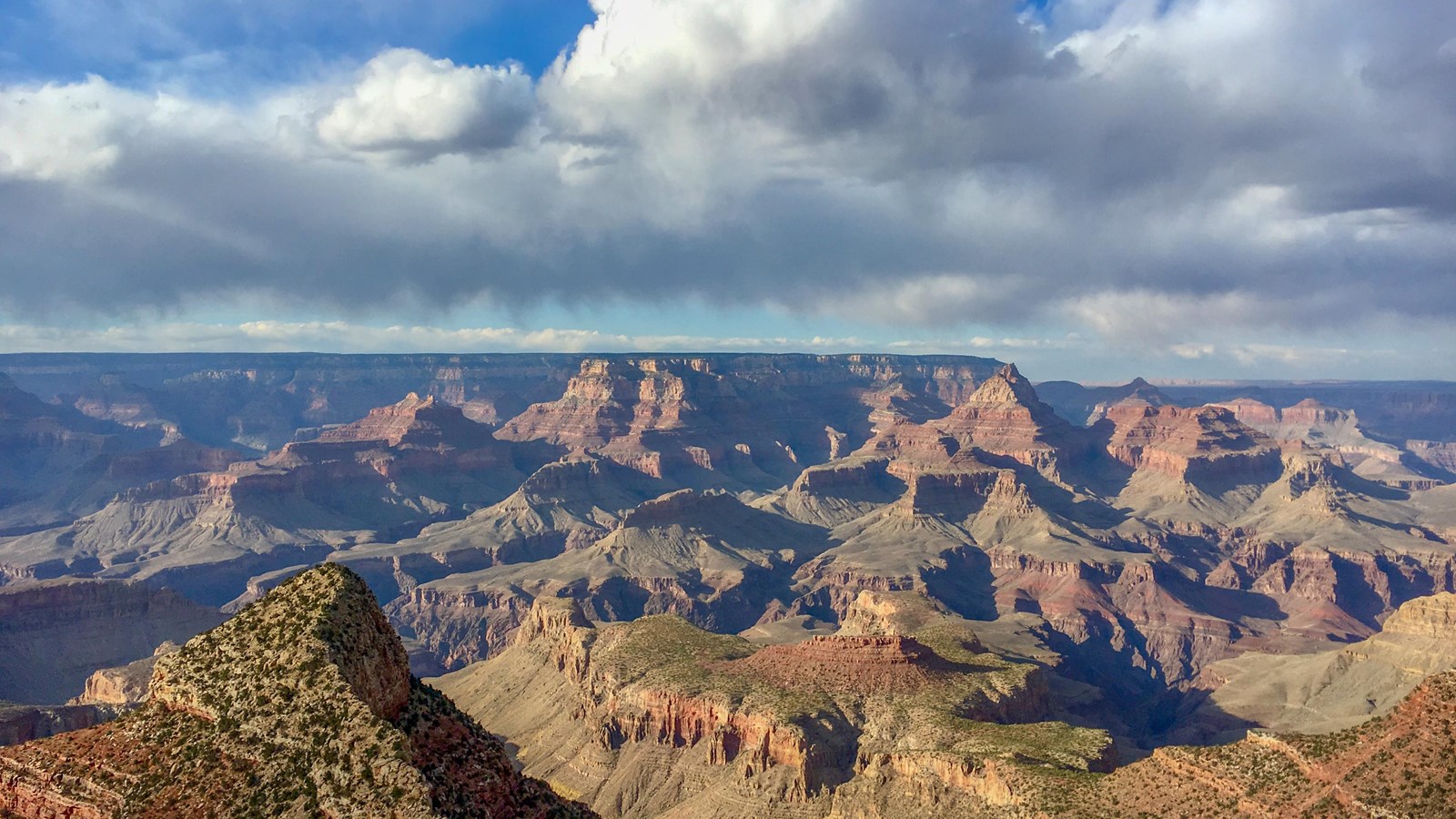 An open scenic canyon vista of colored rocks, steep slopes, sheer cliffs, and blue sky with clouds.