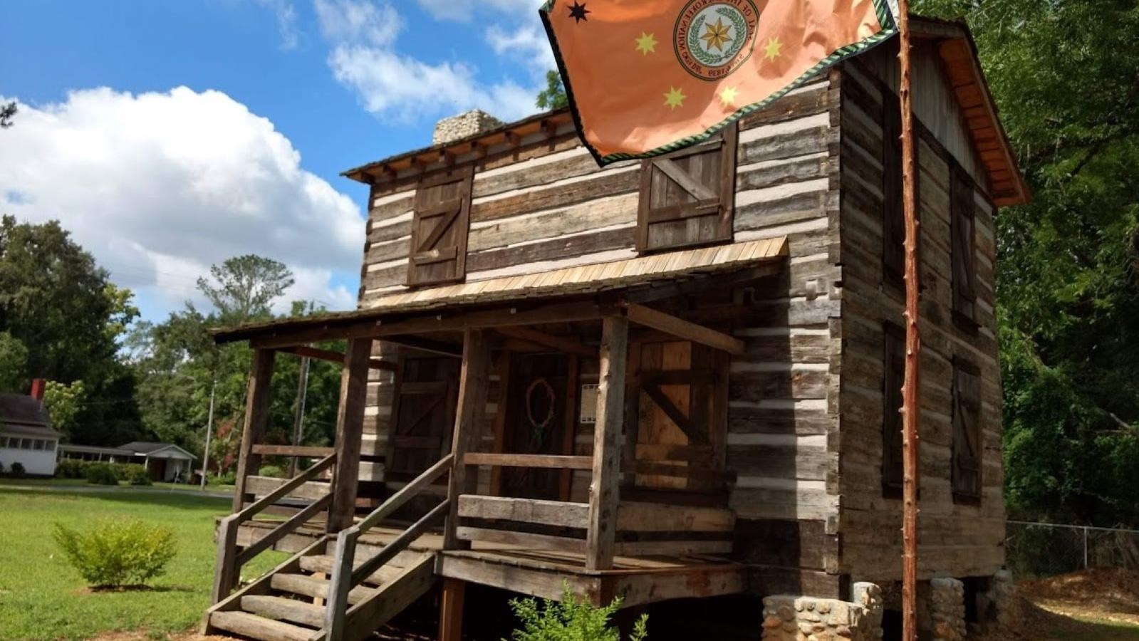 Historic log cabin exterior with orange Cherokee Nation Flag