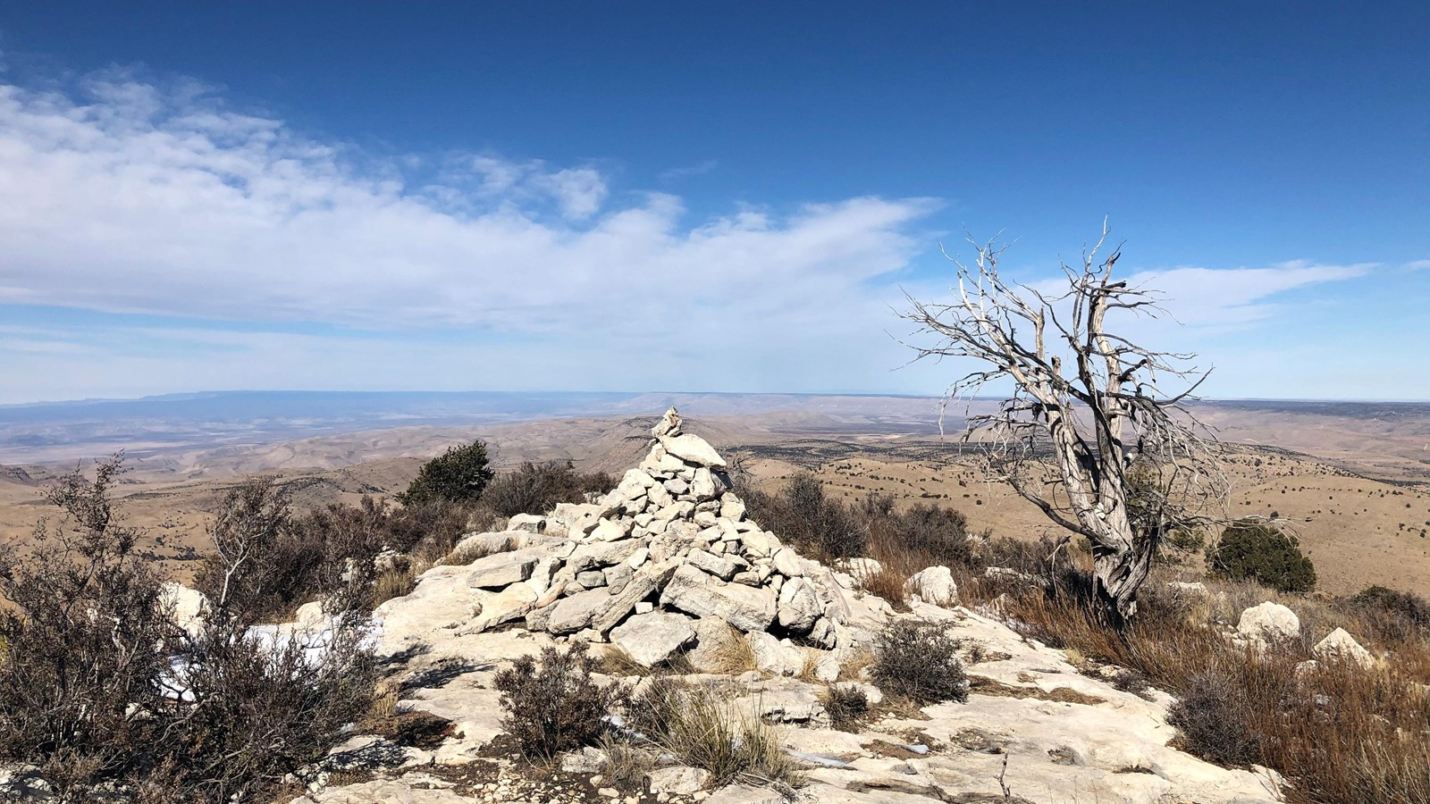 A stone cairn marks a summit with a vast desert landscape beyond