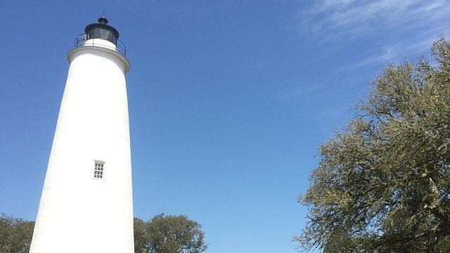 Short, white lighthouse with white fence and surrounding buildings