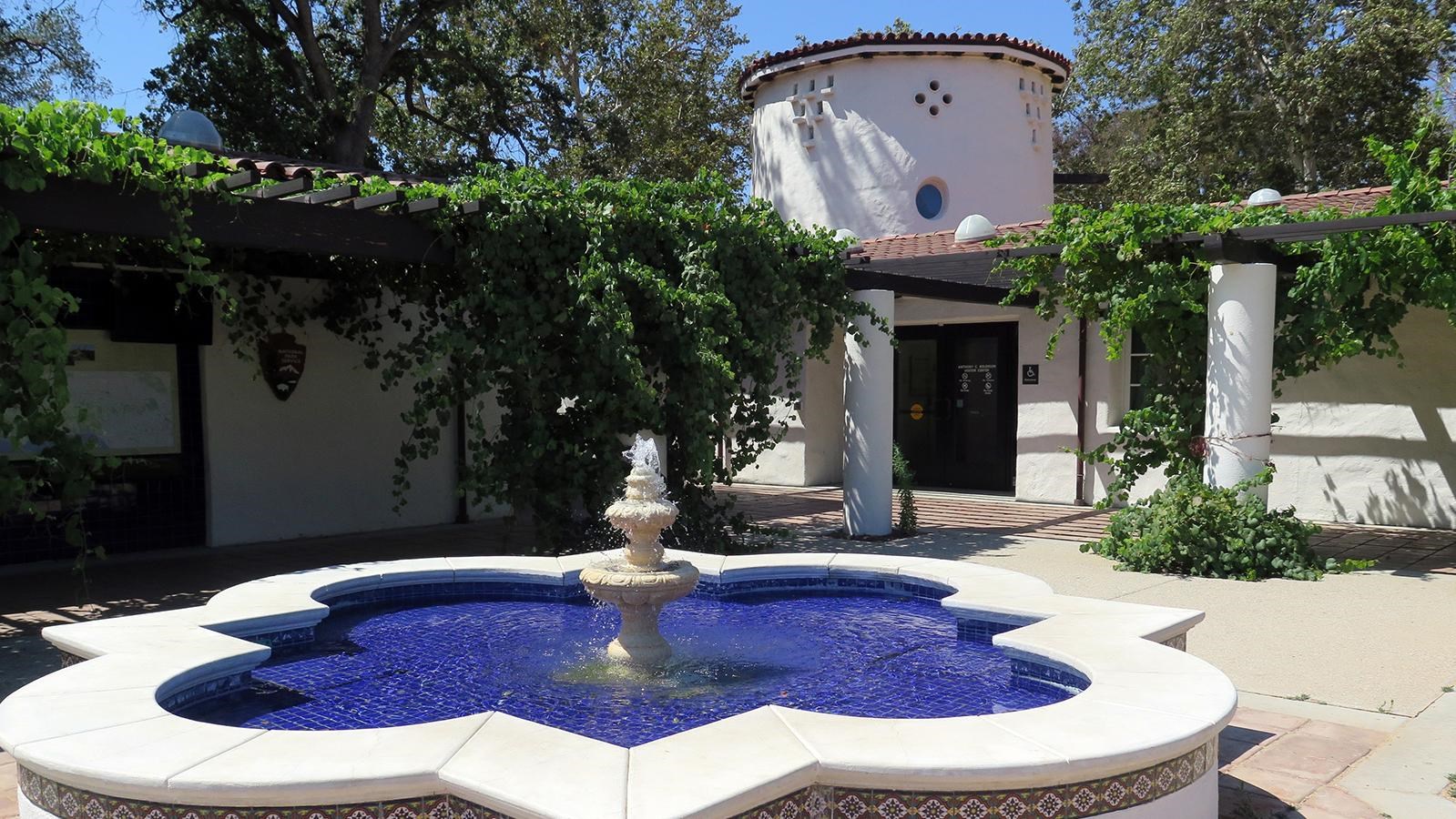 White fountain in a courtyard surrounded by grape vines outside a white building.