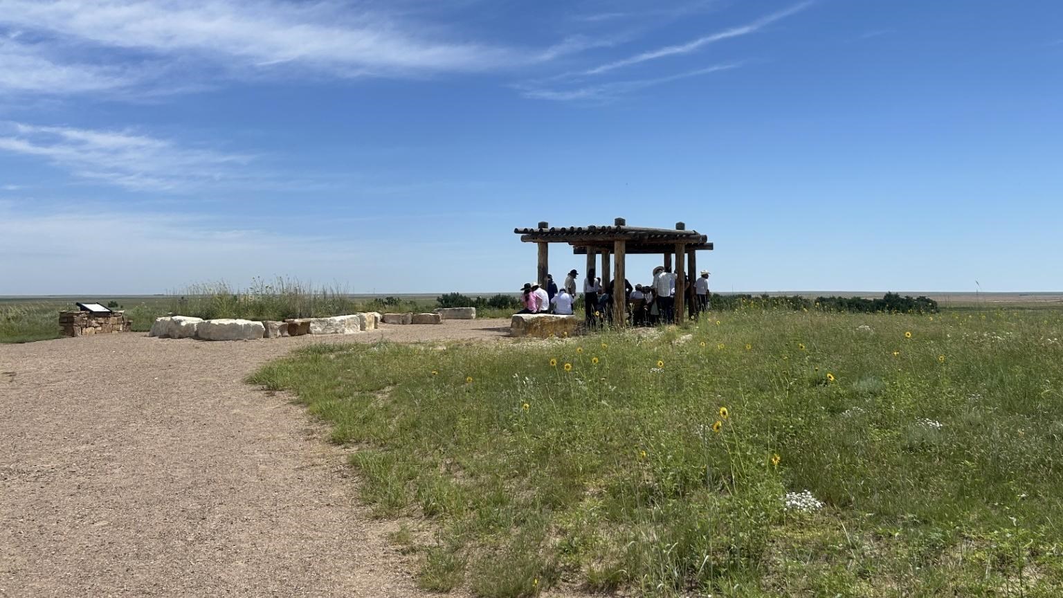 A trail leads to a shade structure with benches at an overlook area in a prairie landscape.