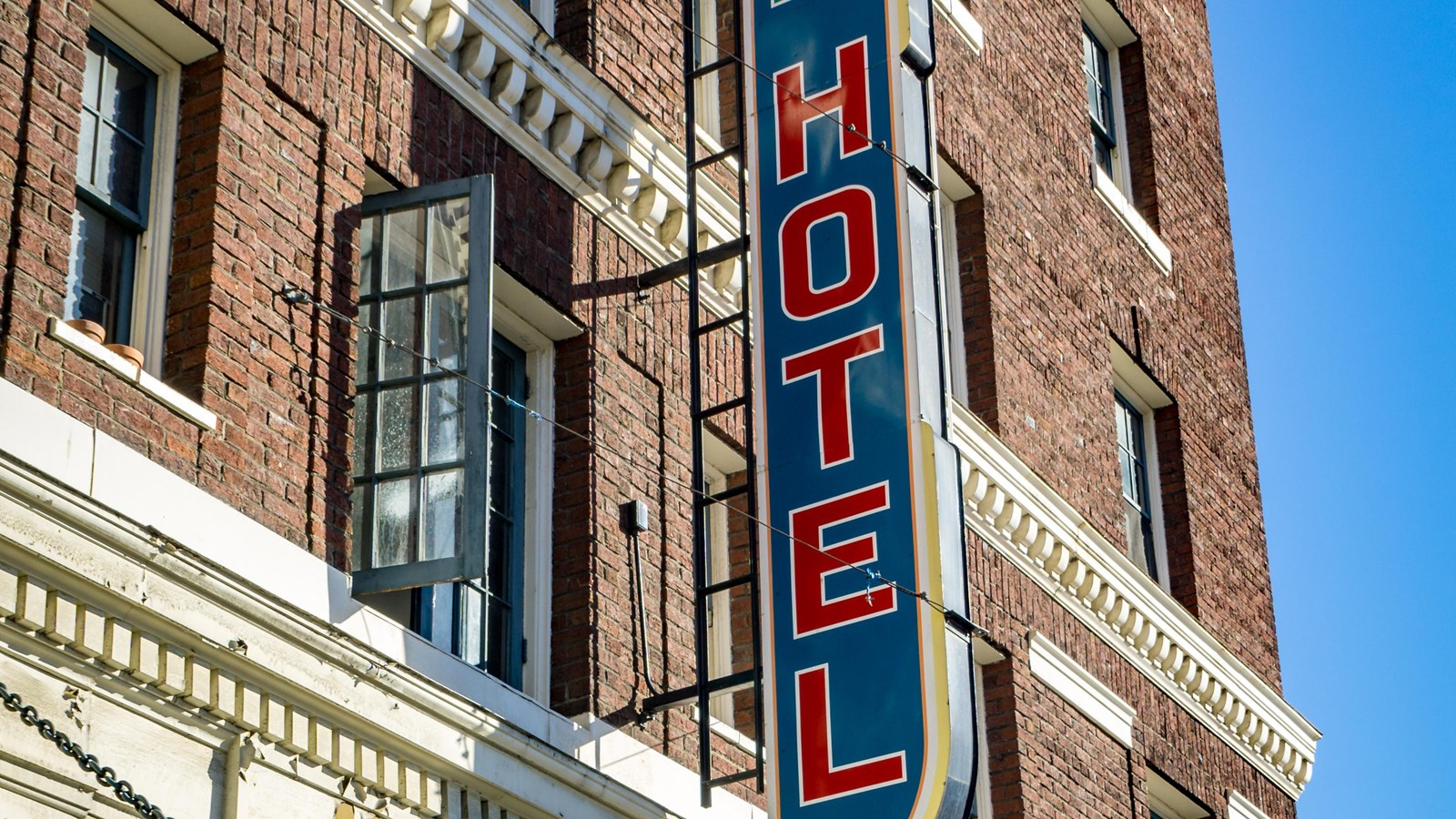 Historical, brick hotel building with a decorative marquee and a large vertical sign.