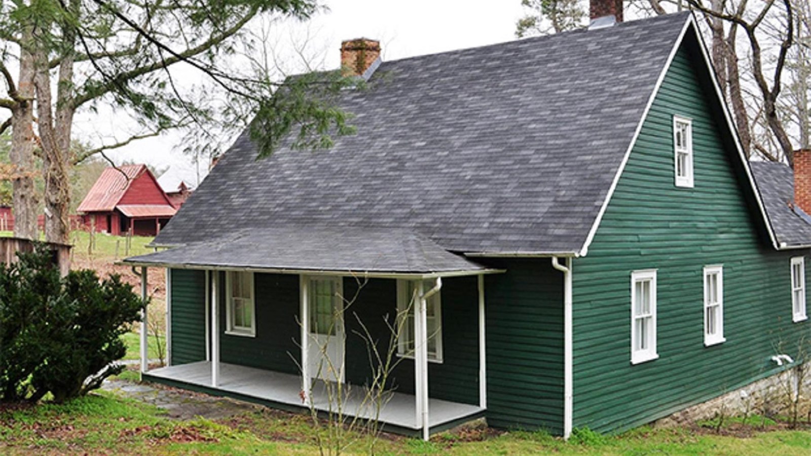 Green farm home with white trim sits on a farm landscape