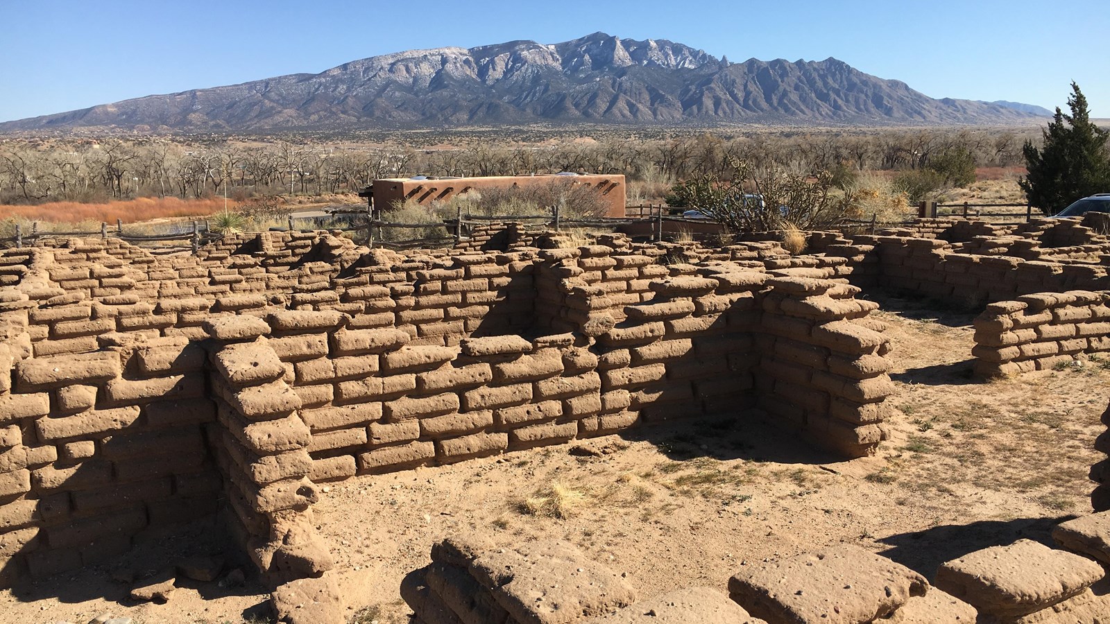 Adobe ruins sit in front of distant snow-dusted desert peaks.
