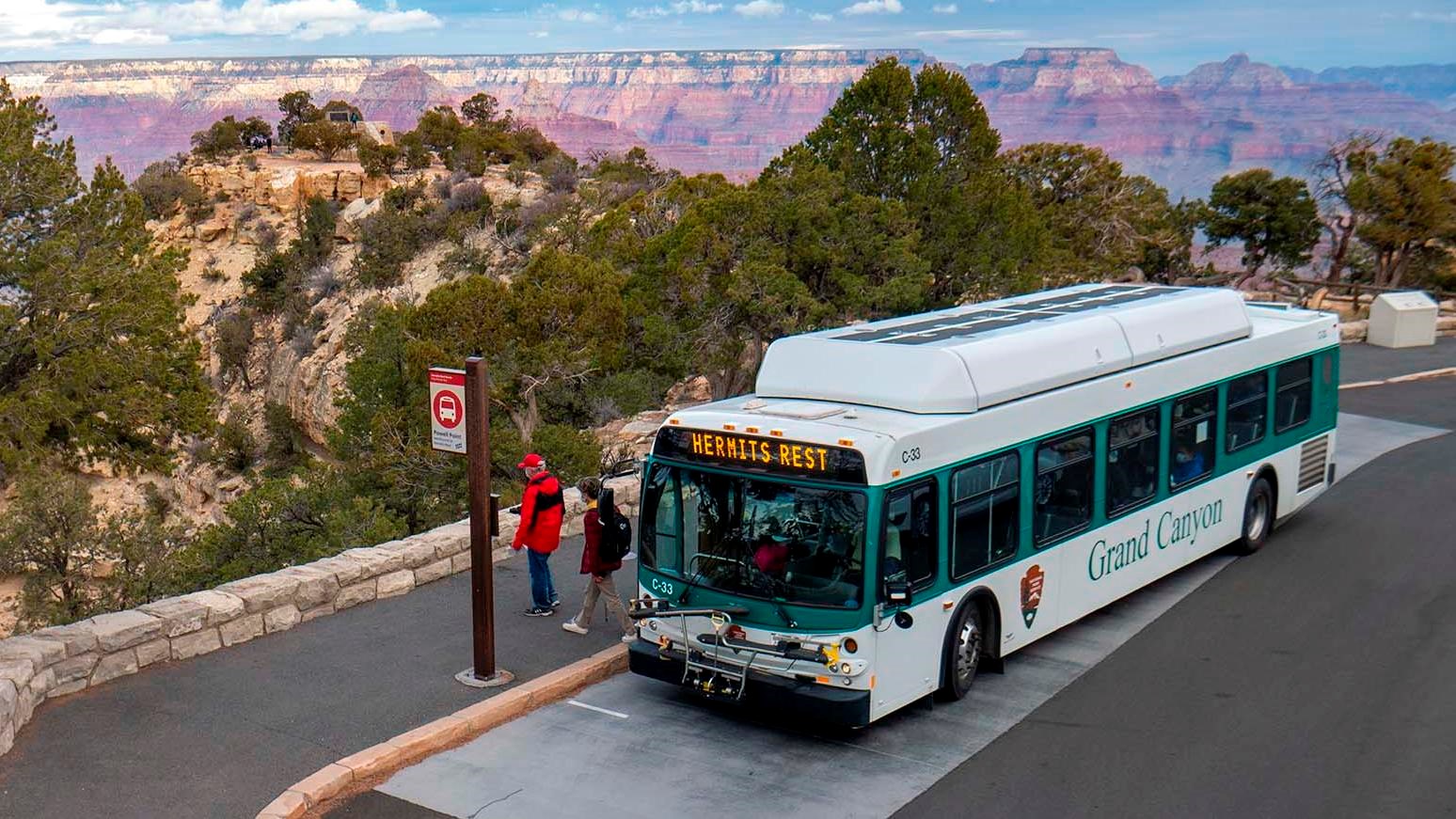 a white and green bus unloading passengers by a low rock wall with the canyon landscape beyond.