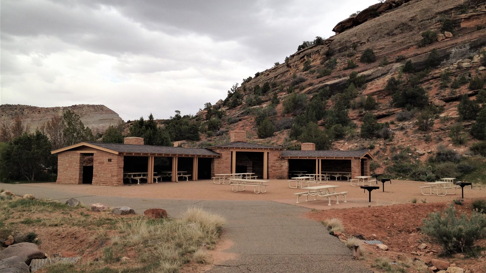 large stone shelter, open facing spacious area with picnic tables and grills, large rocks behind