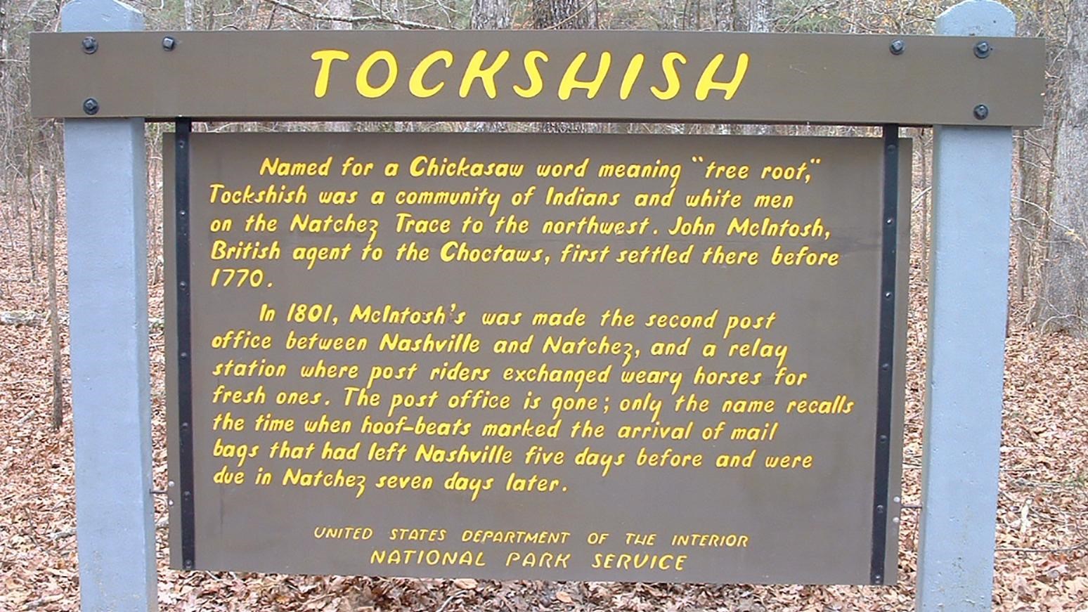 Wooden sign painted brown with yellow letters. Header of sign reads 