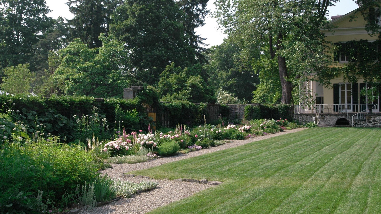 A green lawn surrounded by a tall stone wall and rectangular beds planted with flowers.