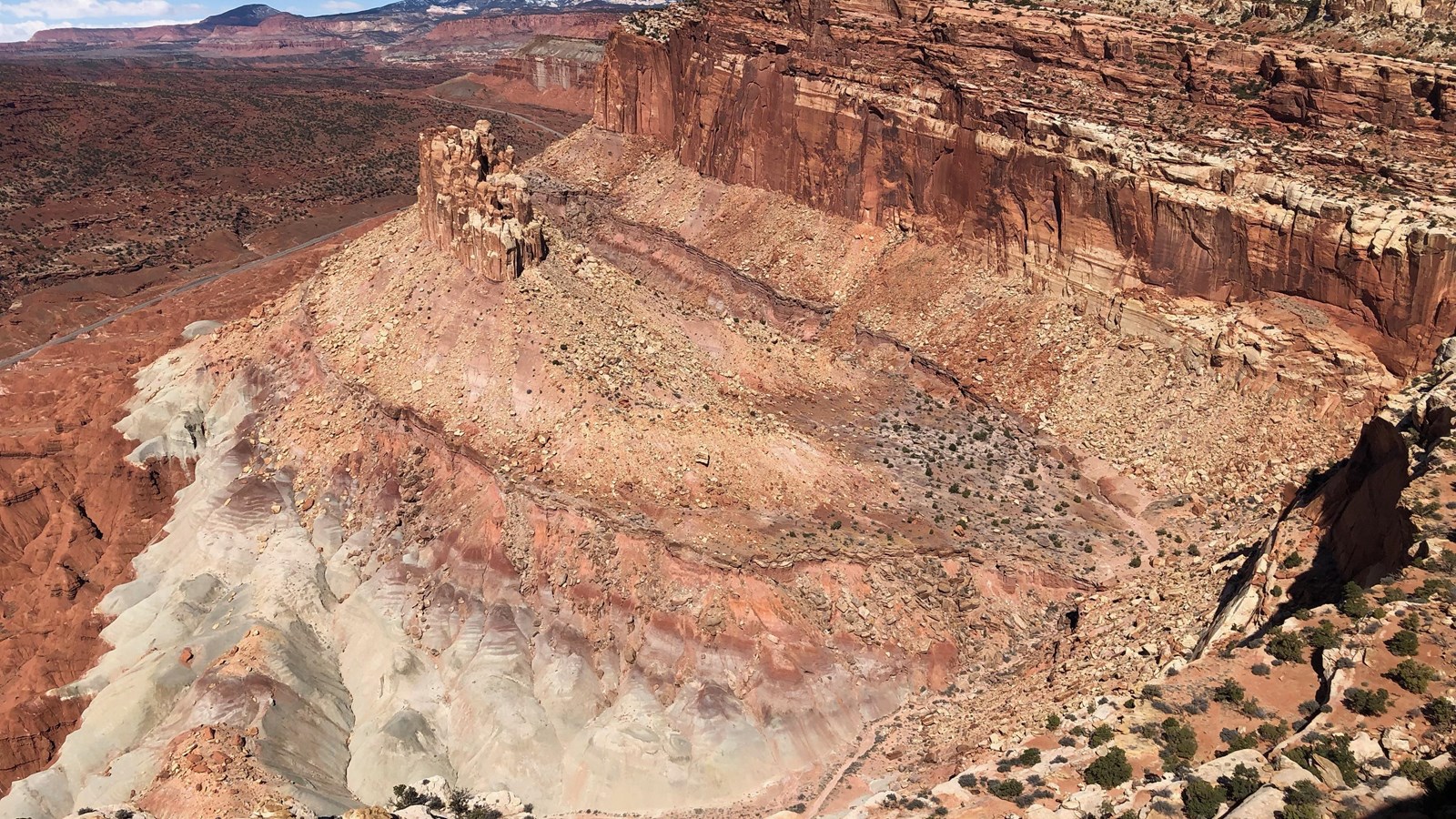 A huge amphitheater of banded cliffs surrounds a standing plinth of sandstone above a highway