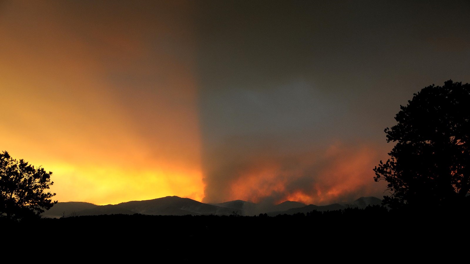 yellow, orange, and black smoke fills the sky against distant mountains