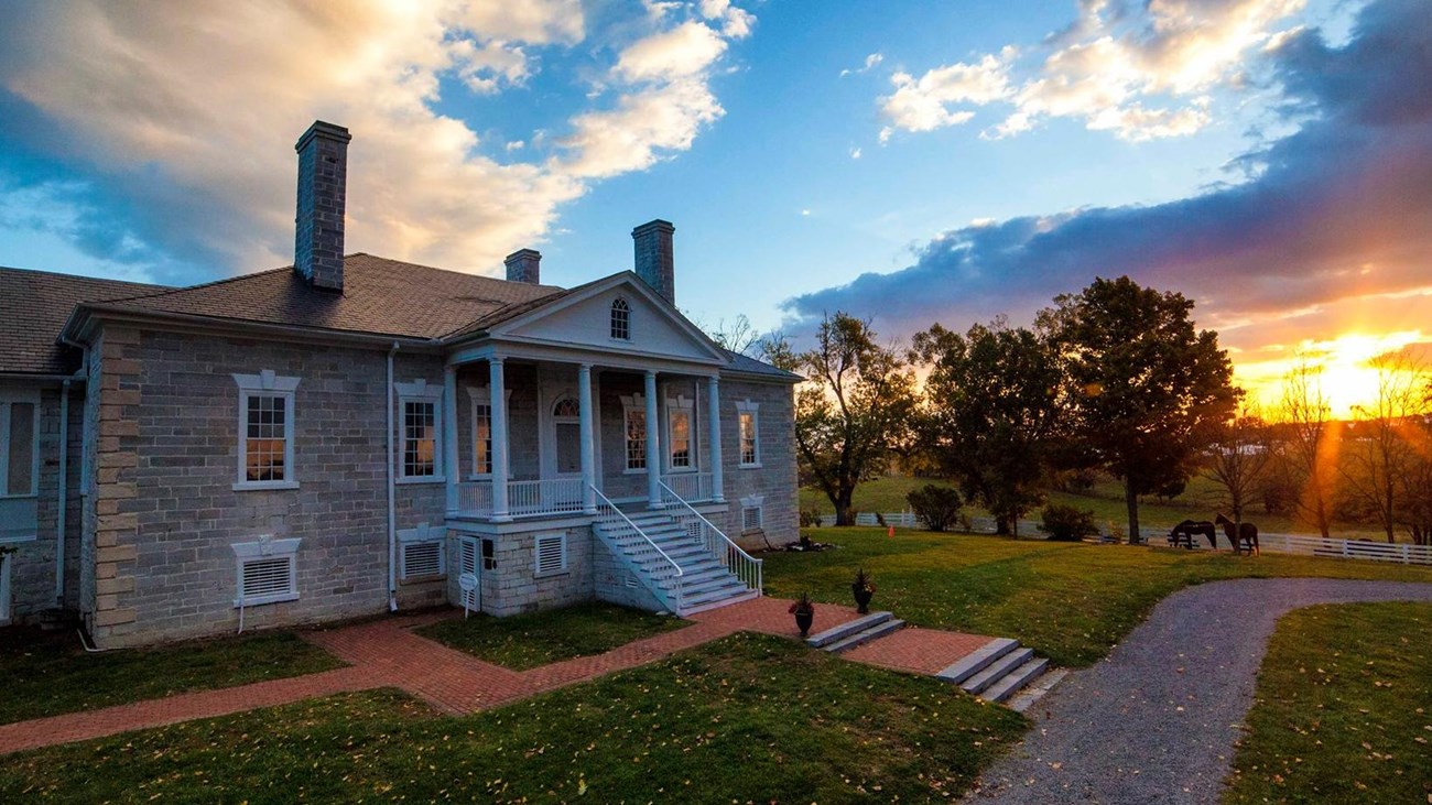 The rising sun lights the clouds over an antebellum stone mansion with a white portico.