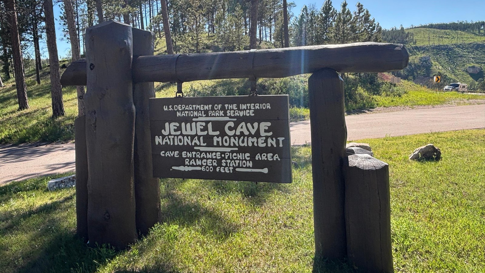 Jewel Cave National Monument\'s wooden entrance sign on a grass median. 