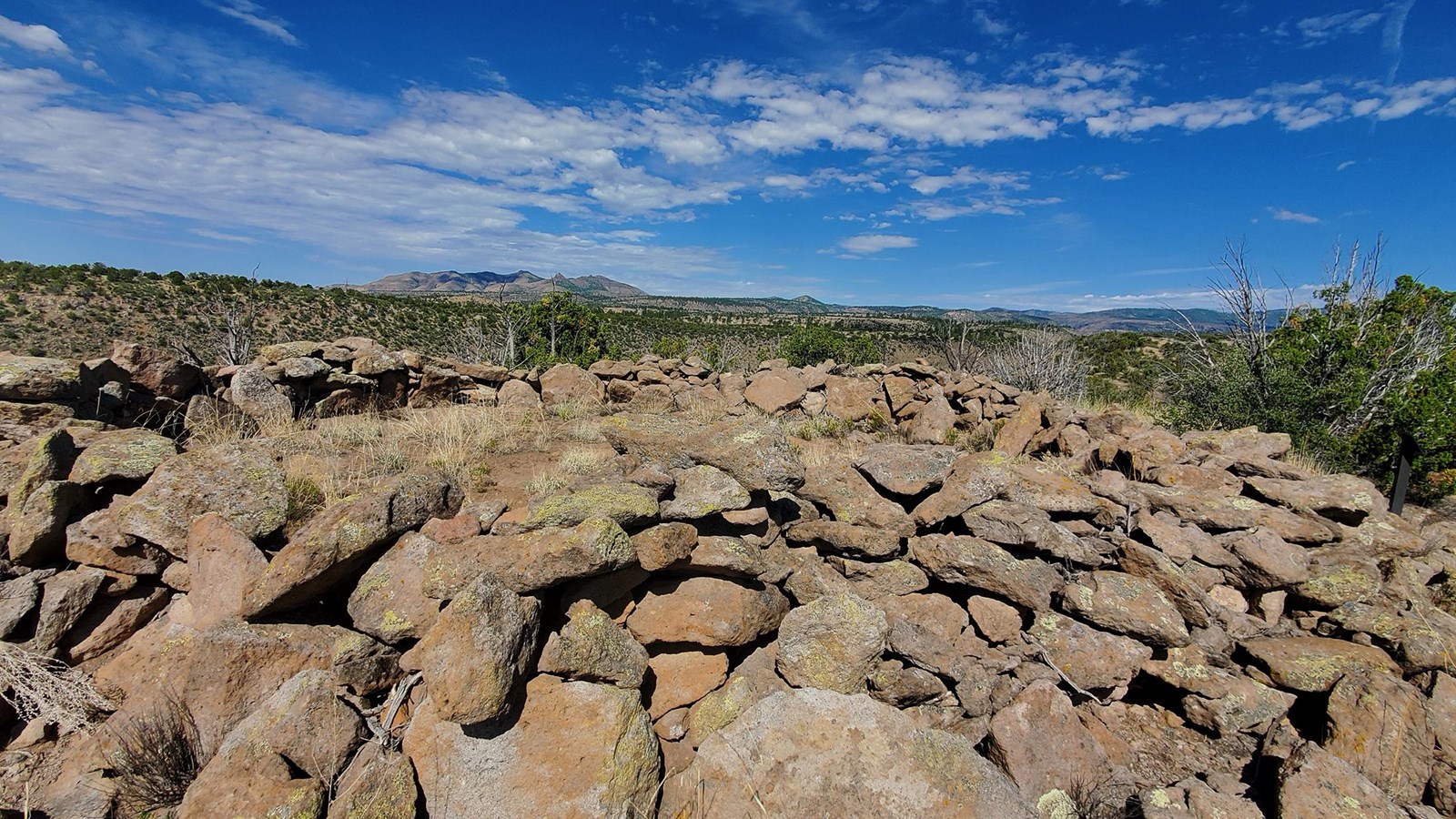 stacked rocks in a structure with distant mountains and blue skies with scattered clouds.