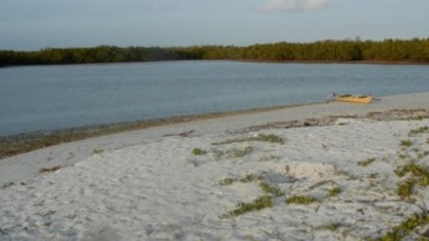 White sand with patches of grass growing through. A yellow kayak is beached on the shore in distance